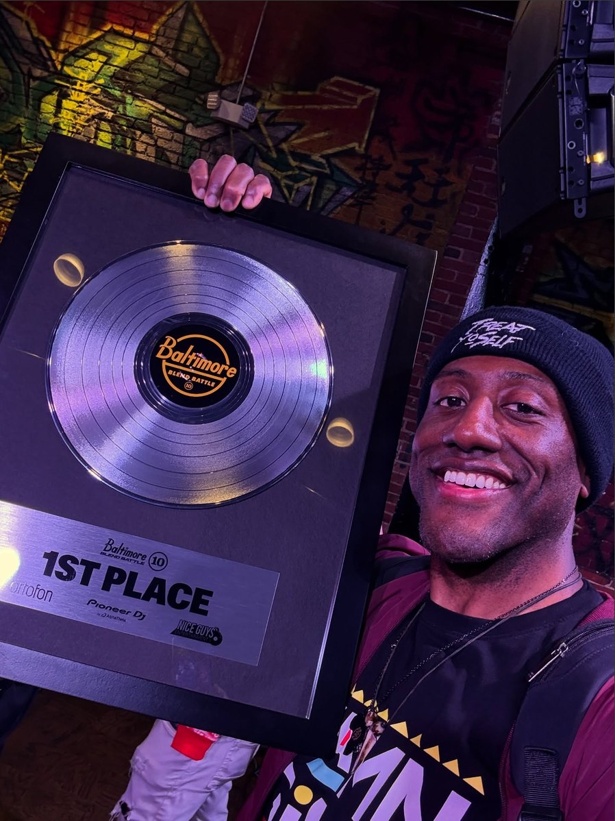 DJ Bizzon holding the Baltimore Blend Battle 10 first place award — a framed platinum record with the BBB 10 logo on the label.